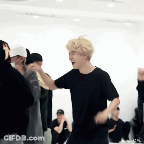 A Man In A Black Shirt Is Laughing While Dancing In A Room With Other People . GIF
