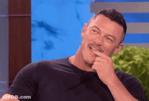 A Man In A Black Shirt Is Laughing With His Hand To His Mouth . GIF