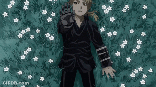 A Man In A Black Shirt Is Laying In A Field Of Flowers GIF