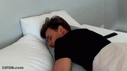 A Man In A Black Shirt Is Laying On A Bed GIF