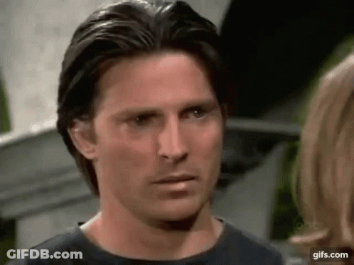 A Man In A Black Shirt Is Looking At A Woman In A Kitchen . GIF