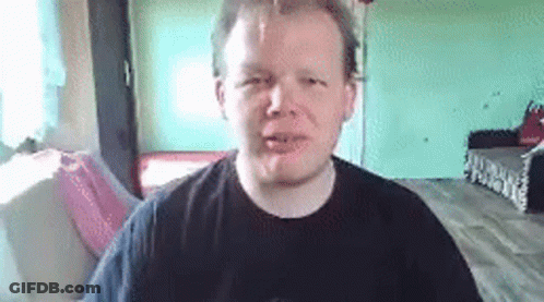 A Man In A Black Shirt Is Making A Funny Face While Sitting In A Living Room . GIF