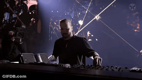 A Man In A Black Shirt Is Playing A Dj Set With A Camera Behind Him GIF