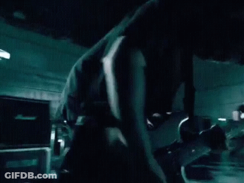 A Man In A Black Shirt Is Playing A Guitar In A Dark Room GIF