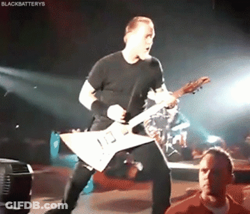 A Man In A Black Shirt Is Playing A Guitar On A Stage GIF