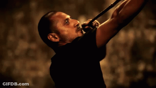 A Man In A Black Shirt Is Playing A Trumpet In A Dark Room GIF
