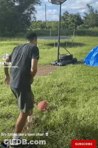 A Man In A Black Shirt Is Playing Basketball In A Field With A Trampoline In The Background GIF