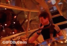 A Man In A Black Shirt Is Playing Drums In A Room . GIF