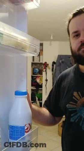 A Man In A Black Shirt Is Reaching Into A Fridge To Take A Bottle Of Milk GIF