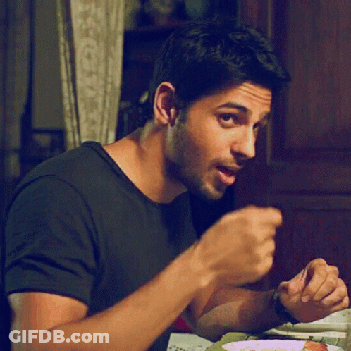 A Man In A Black Shirt Is Sitting At A Table And Eating Food GIF