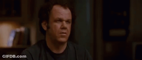 A Man In A Black Shirt Is Sitting At A Table In A Dark Room . GIF