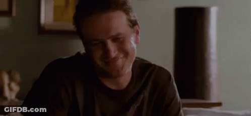 A Man In A Black Shirt Is Sitting At A Table In A Living Room And Smiling . GIF
