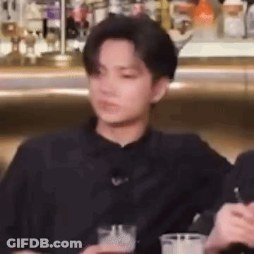 A Man In A Black Shirt Is Sitting At A Table With A Drink In His Hand . GIF