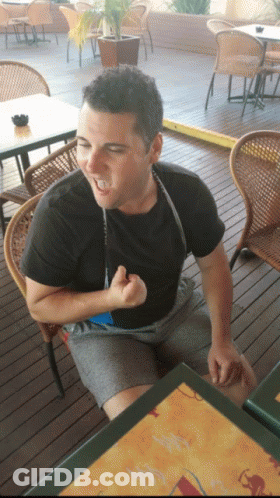 A Man In A Black Shirt Is Sitting At A Table With A Menu On It GIF