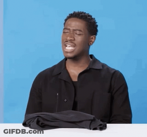 A Man In A Black Shirt Is Sitting At A Table With His Eyes Closed And A Black Shirt On His Lap . GIF