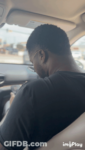 Man In Black Shirt Sitting In Car Looking At Phone GIF