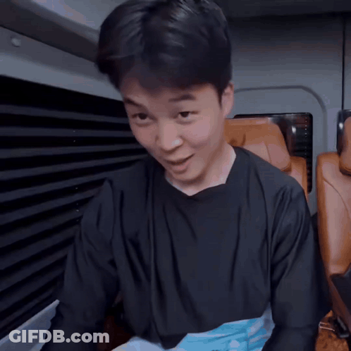 A Man In A Black Shirt Is Sitting In A Car With A Foreign Language Behind Him GIF
