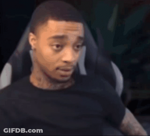 A Man In A Black Shirt Is Sitting In A Chair And Looking At The Camera . GIF