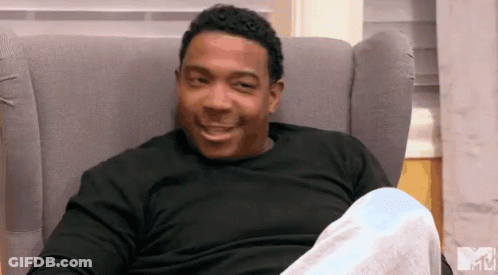 A Man In A Black Shirt Is Sitting In A Chair With A Mtv Logo In The Background GIF