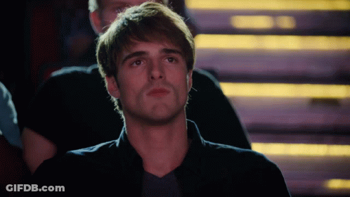 A Man In A Black Shirt Is Sitting In A Dark Room With Stairs In The Background GIF