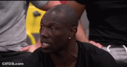 A Man In A Black Shirt Is Sitting In A Gym With A Group Of People Behind Him . GIF