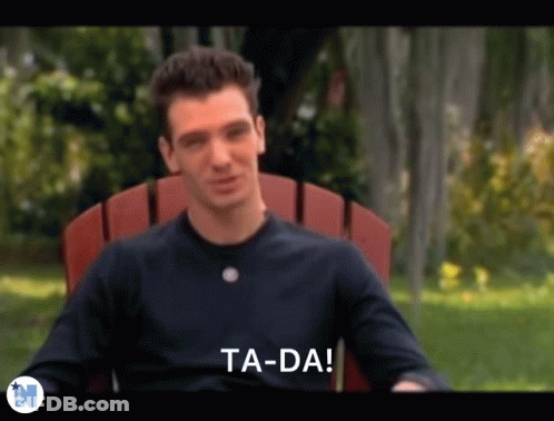 A Man In A Black Shirt Is Sitting In A Red Chair And Says Ta-Da . GIF