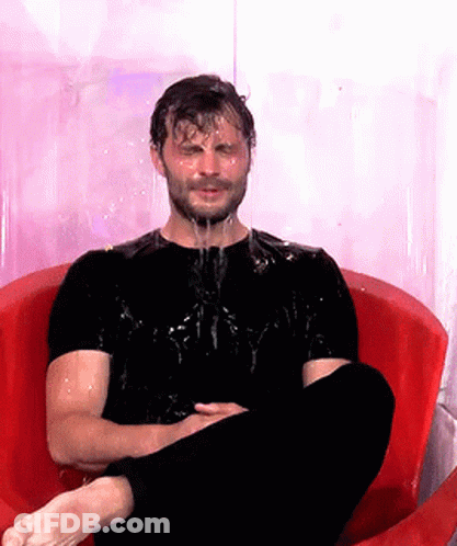 A Man In A Black Shirt Is Sitting In A Red Chair With Water Dripping Off His Face GIF