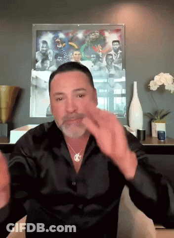 A Man In A Black Shirt Is Sitting In Front Of A Framed Picture GIF
