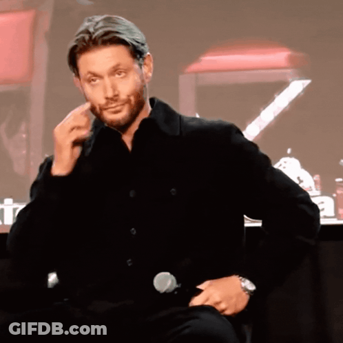 A Man In A Black Shirt Is Sitting In Front Of A Microphone And Making A Face GIF
