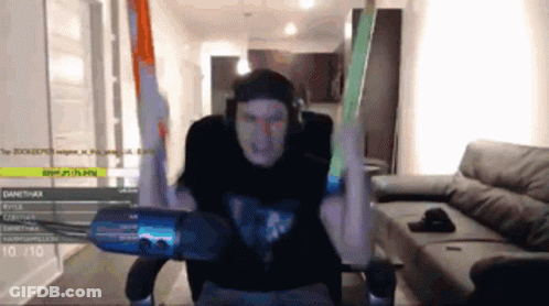 A Man In A Black Shirt Is Sitting In Front Of A Microphone With His Arms In The Air . GIF
