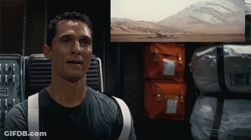 A Man In A Black Shirt Is Sitting In Front Of A Screen With A Picture Of A Desert On It GIF
