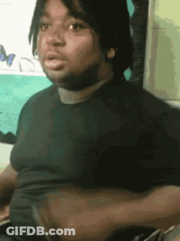 A Man In A Black Shirt Is Sitting In Front Of A Wall With Butterflies On It GIF