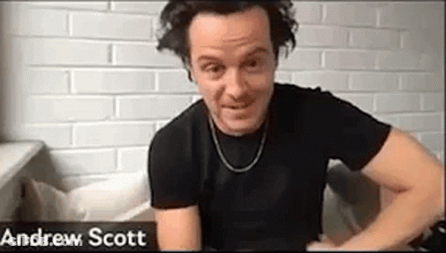 A Man In A Black Shirt Is Sitting On A Couch In Front Of A Brick Wall . GIF