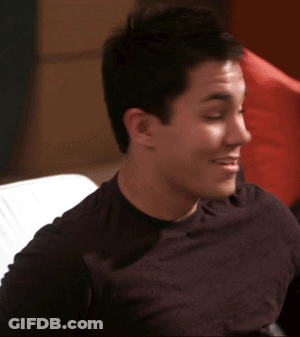 A Man In A Black Shirt Is Sitting On A Couch Smiling GIF
