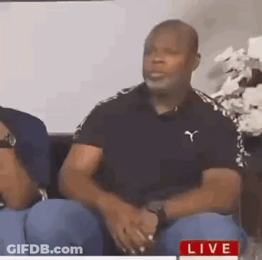 A Man In A Black Shirt Is Sitting On A Couch With A Woman . GIF