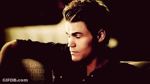 A Man In A Black Shirt Is Sitting On A Couch With His Head Resting On His Arm GIF