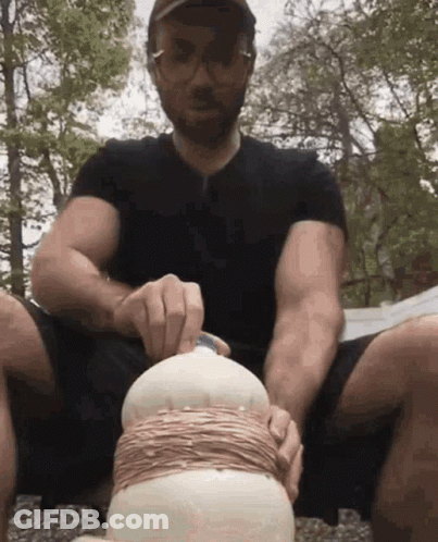 A Man In A Black Shirt Is Sitting On The Ground Holding A Bottle GIF