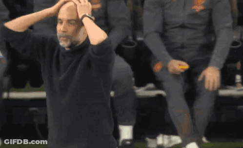 A Man In A Black Shirt Is Sitting On The Ground With His Hands On His Head . GIF