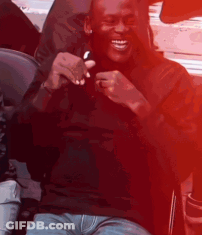 A Man In A Black Shirt Is Smiling And Holding A Cell Phone GIF