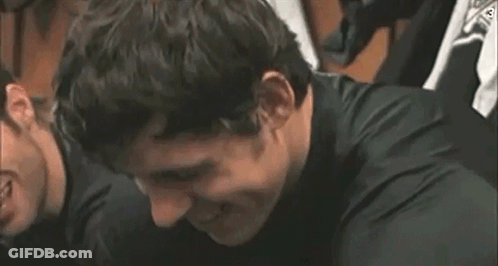 A Man In A Black Shirt Is Smiling And Looking At The Camera . GIF