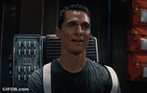 A Man In A Black Shirt Is Smiling In Front Of A Box That Says Aaa GIF