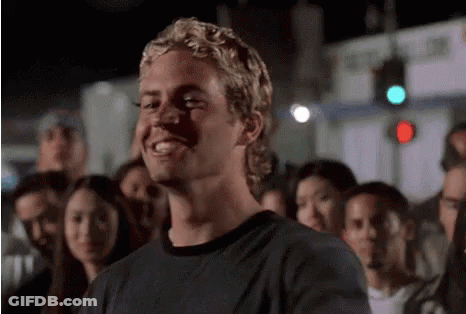 A Man In A Black Shirt Is Smiling In Front Of A Crowd . GIF