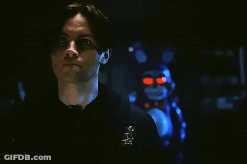 A Man In A Black Shirt Is Smiling In Front Of A Stuffed Animal That Has Red Eyes GIF