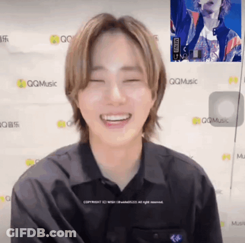 A Man In A Black Shirt Is Smiling In Front Of A Wall That Says Qqmusic GIF