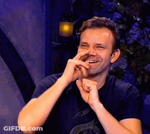 A Man In A Black Shirt Is Smiling While Holding His Hand To His Nose . GIF