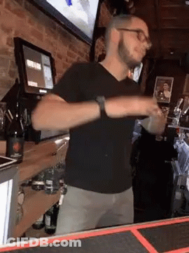 A Man In A Black Shirt Is Standing At A Bar . GIF