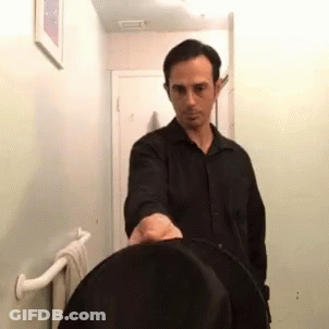 A Man In A Black Shirt Is Standing In A Bathroom With A Towel Rack . GIF