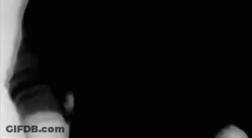 A Man In A Black Shirt Is Standing In A Black And White Photo . GIF