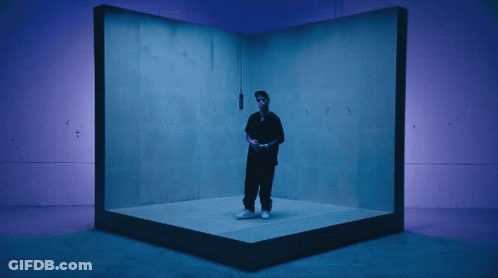 A Man In A Black Shirt Is Standing In A Blue Room GIF