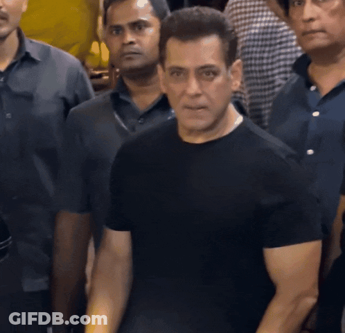 A Man In A Black Shirt Is Standing In A Crowd Of People GIF